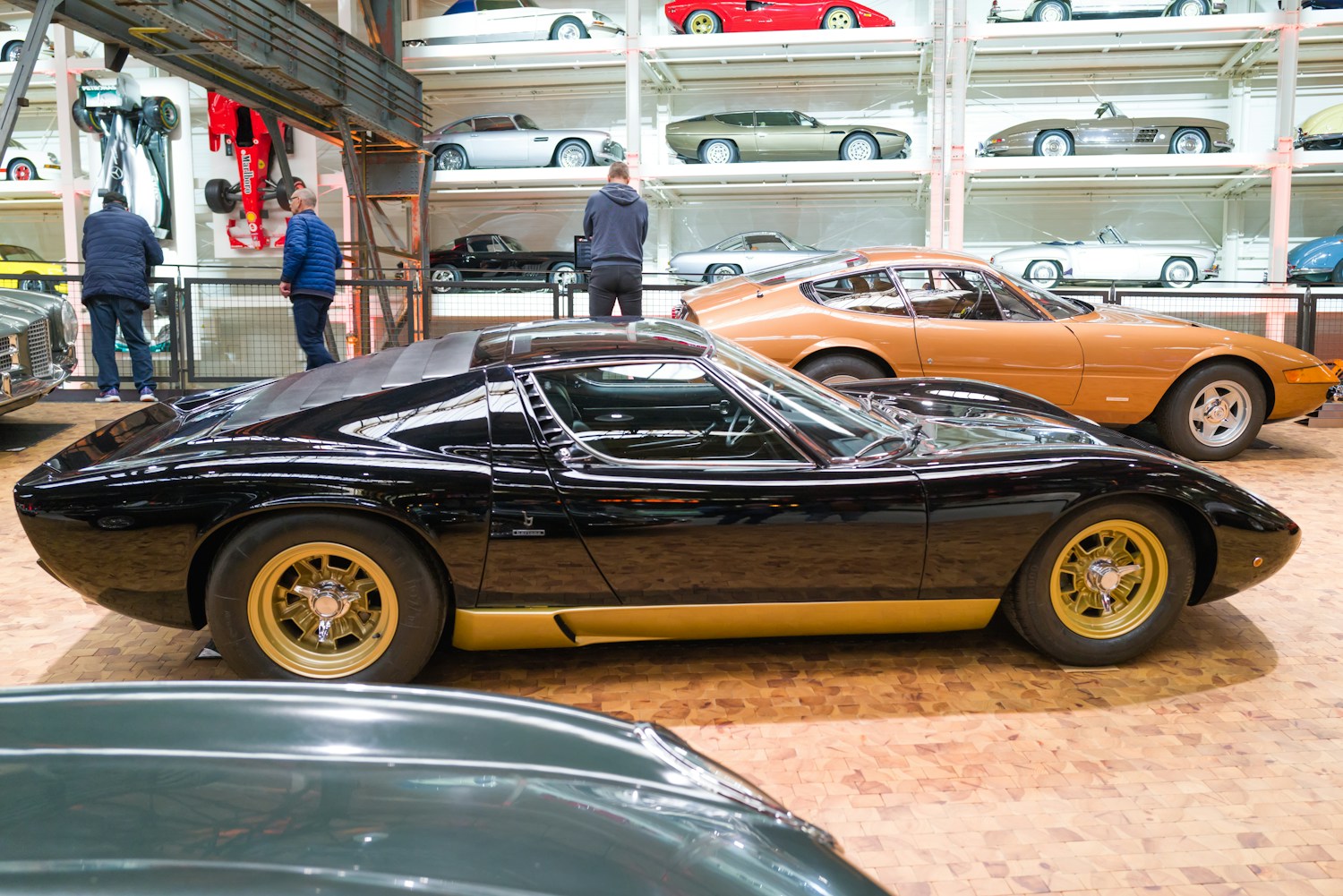 A black Lamborghini Miura with gold wheels alongside an orange Miura in a car collection